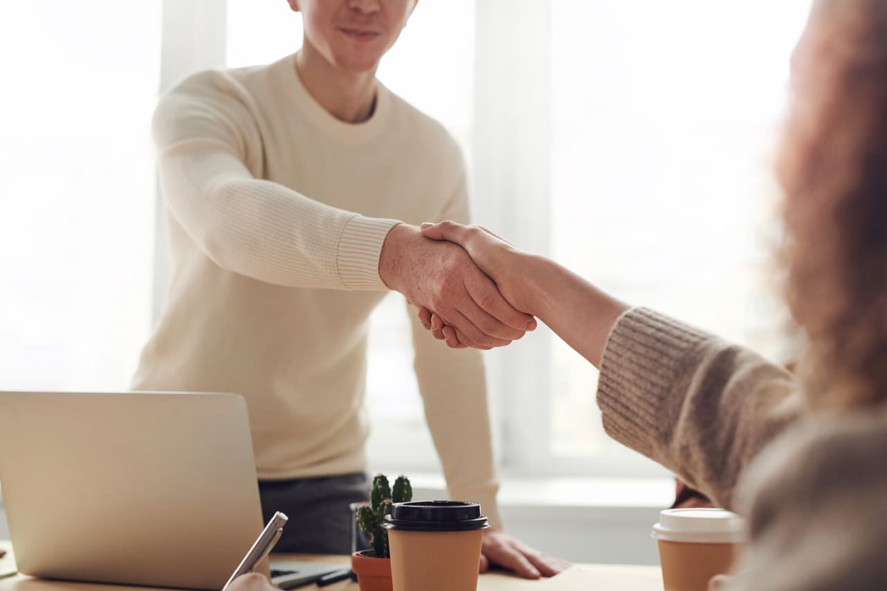 a landlord in a white shirt reaches over their desk to shake the hand of their new tenant