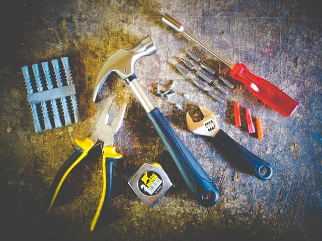 a bunch of tools laid out on a counter like nails, pliers, a tap measure, a hammer, a screw driver, and a wrench